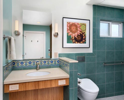 A universal design bathroom inspired by Catalina tiles features a wall-mounted toilet and a roll-under vanity.