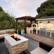 Firepit seating area next to outdoor kitchen with grill and pizza oven