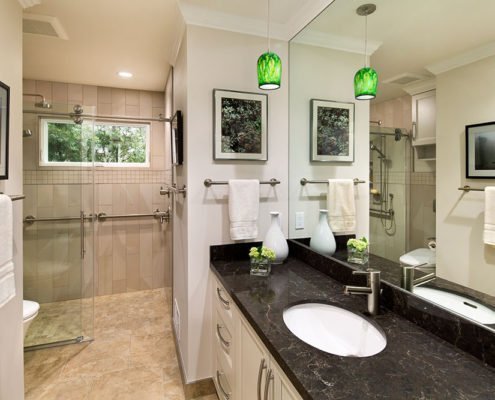 A contemporary universal design bathroom features a curbless shower and brushed silver railings.