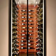 A modern wine cellar is illuminated from the back and showcased through glass doors