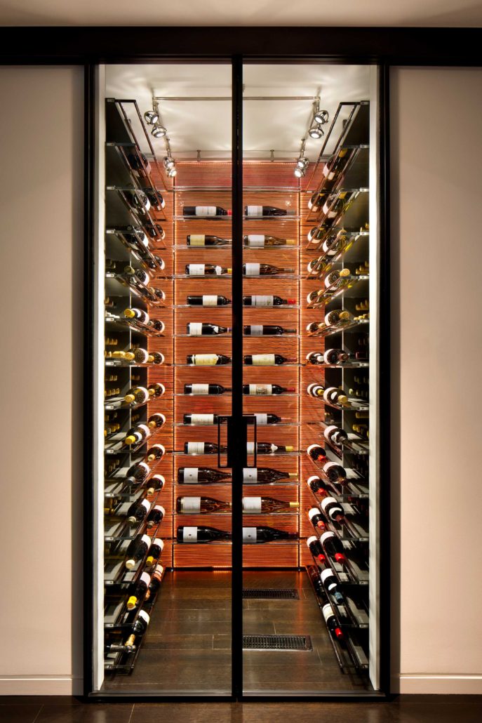 A modern wine cellar is illuminated from the back and showcased through glass doors