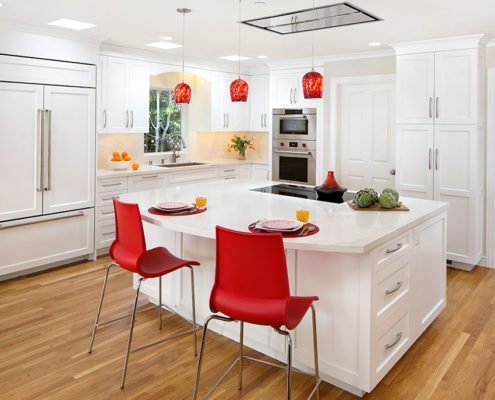A light-filled kitchen adds pops of red against an otherwise white color palette.