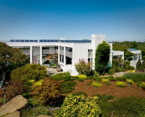 A view of the rear of a modern, two story home in Los Altos Hills with solar panels on the roof.