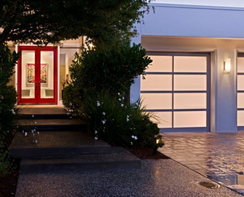 The front entry of a modern Los Altos Hills home is surrounded by lush foliage, making its red front door pop.