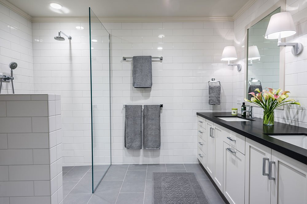 A monochromatic universal design bathroom has a curbless shower with a glass wall and dual sinks.