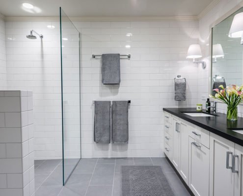 A monochromatic universal design bathroom has a curbless shower with a glass wall and dual sinks.