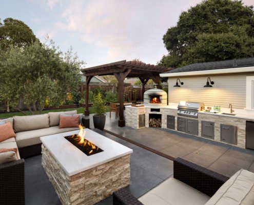 Firepit seating area next to outdoor kitchen with grill and pizza oven