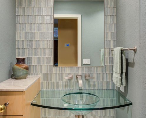 A contemporary Cupertino bathroom features a full tiled backsplash and glass vanity.