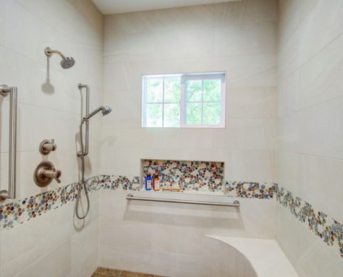 A roll-in shower features two shower heads, multiple hand railings, and a bench.