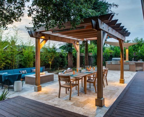 A pergola covers an outdoor dining area near a firepit and lounge seating.