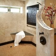 A natural, universal design bathroom features a large, open curbless shower with a bench and brushed handrail in the corner.