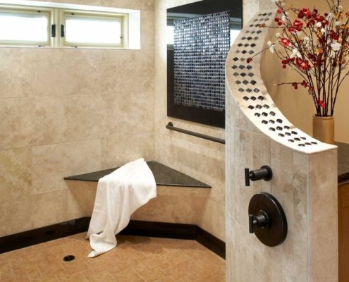 A natural, universal design bathroom features a large, open curbless shower with a bench and brushed handrail in the corner.