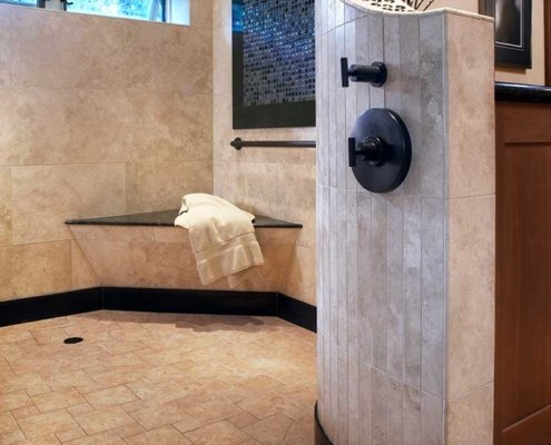 A universal design bathroom has a large, open curbless shower with a bench and brushed handrail in the corner.