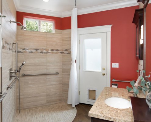 A universal design bathroom features a corner curbless shower with two shower heads, hand rails, and a roll-under vanity.