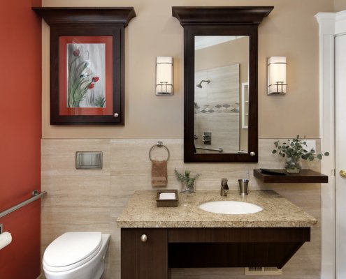 A universal design bathroom has a wall-mounted toilet with a flush plate and roll-under vanity.
