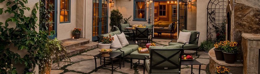 A Tuscan-inspired outdoor courtyard with a stone fireplace, wrought-iron seating, and string lights.