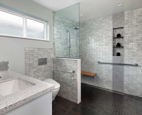 A modern, gray universal design bathroom features a curbless shower and tile details.