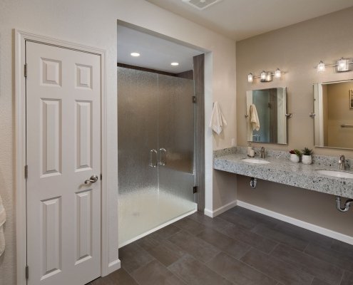 A contemporary universal design bathroom features a curbless shower with closed, frosted glass doors and a roll-under vanity with two sinks.