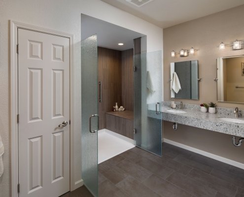 A contemporary universal design bathroom features a curbless shower with open, frosted glass doors and a roll-under vanity with two sinks.