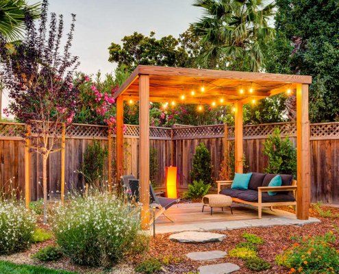 A wooden pergola with string lights covers an outdoor seating area.