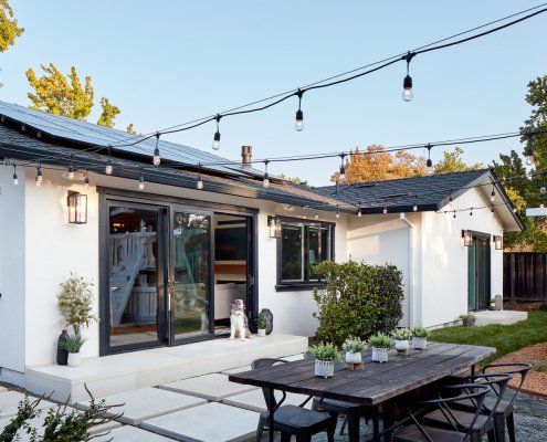 A San Jose backyard has large concrete pavers, a dining area, and plenty of string lighting.