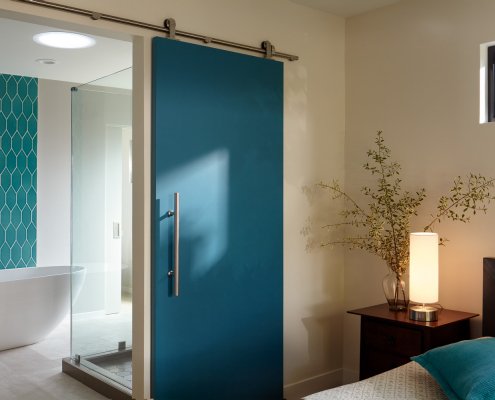 A serene bedroom in San Jose adds a modern pop of blue on a barn door to the bathroom.