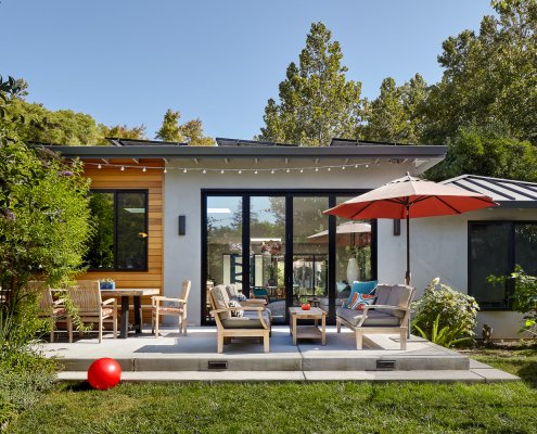 A concrete deck outside of a modern home provides space for a dining table, seating area, and umbrella.